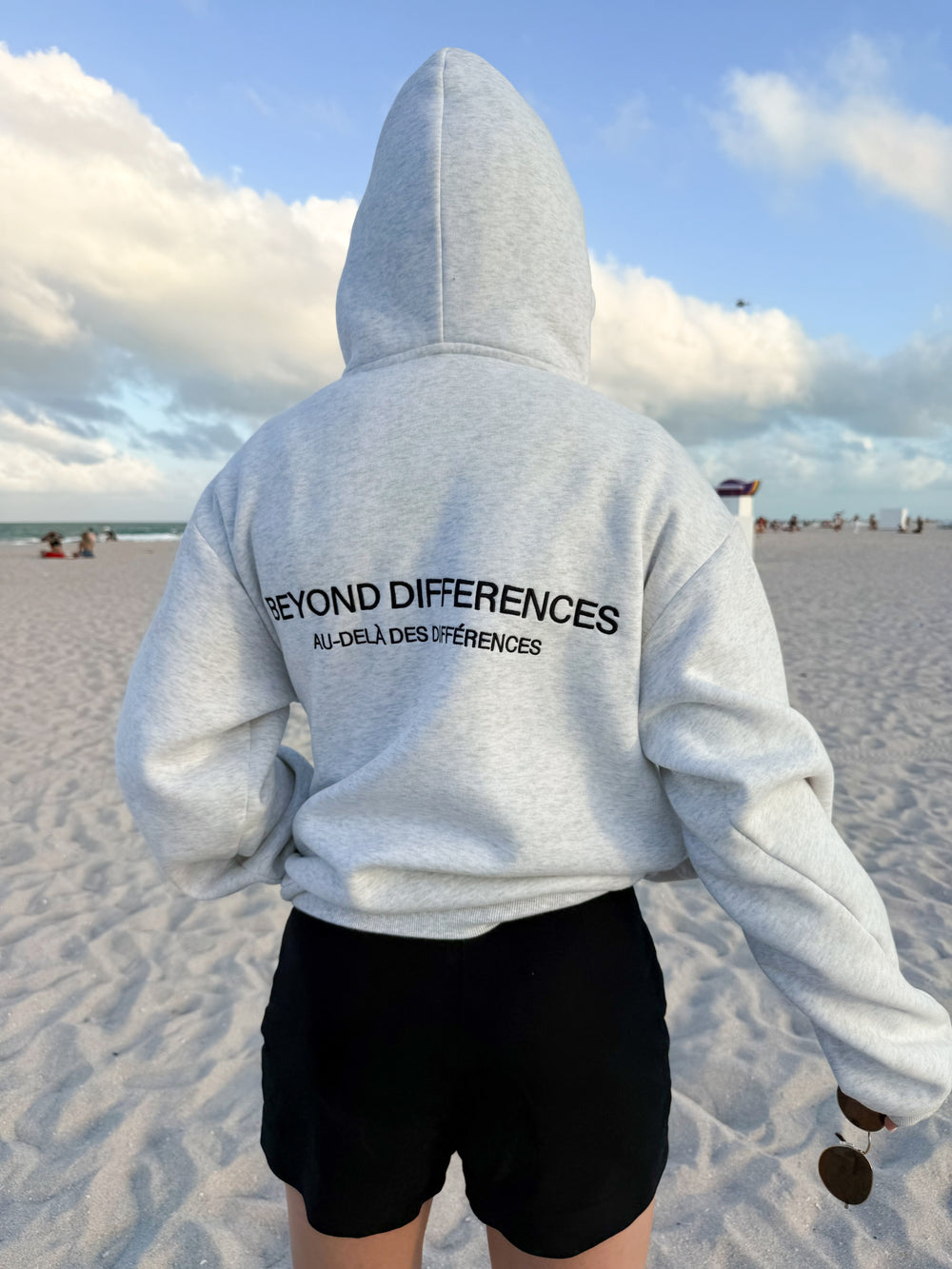 Person on the beach seen from behind in the grey Heavyweight Hoodie, hood up