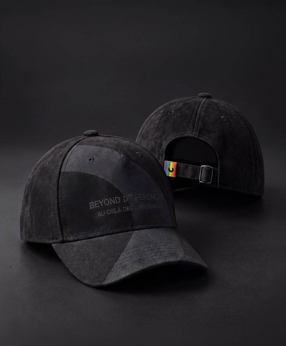 Two black vegan suede caps, BEYOND DIFFERENCES embroidery on the front and rainbow tag at the back