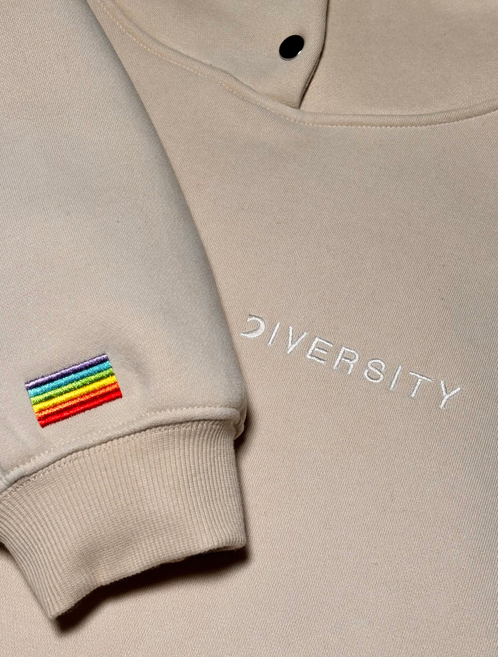 Gros plan du Heavyweight Hoodie Beige : drapeau arc-en-ciel brodé sur la manche et logo DIVERSITY blanc