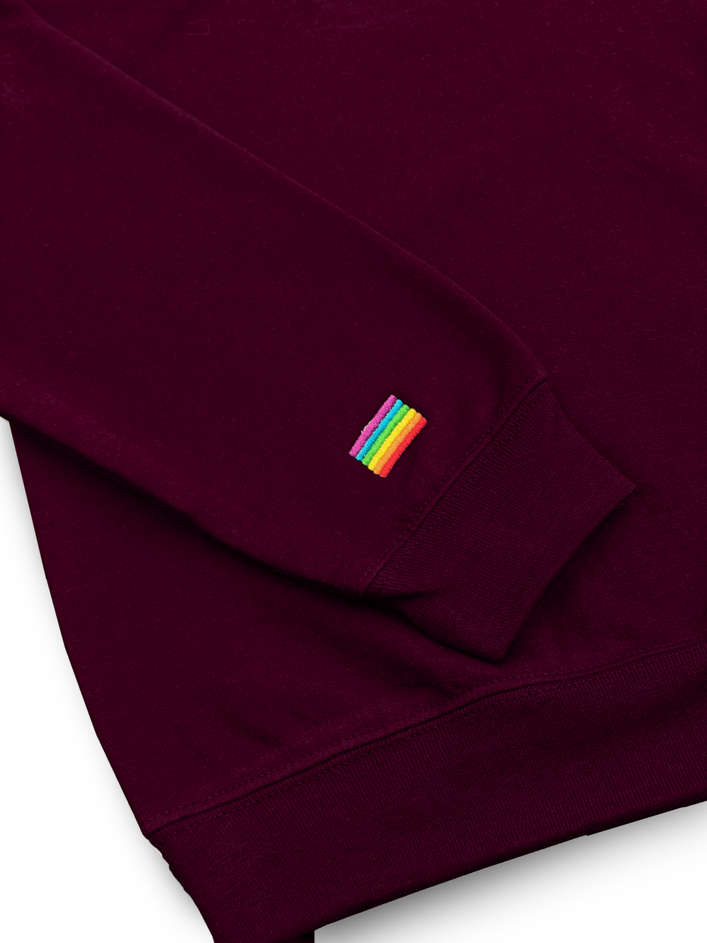 Gros plan du drapeau arc-en-ciel brodé au poignet du chandail 1/4 zip bourgogne