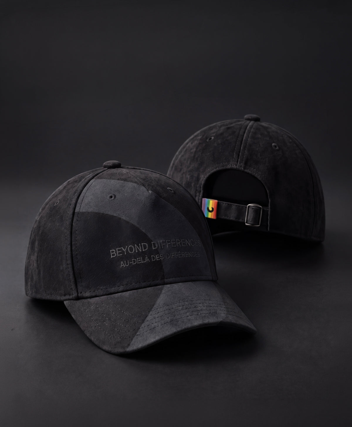 Two black vegan suede caps, BEYOND DIFFERENCES embroidery on the front and rainbow tag at the back