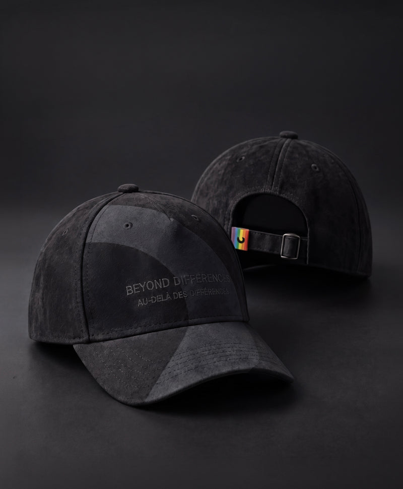 Two black vegan suede caps, BEYOND DIFFERENCES embroidery on the front and rainbow tag at the back