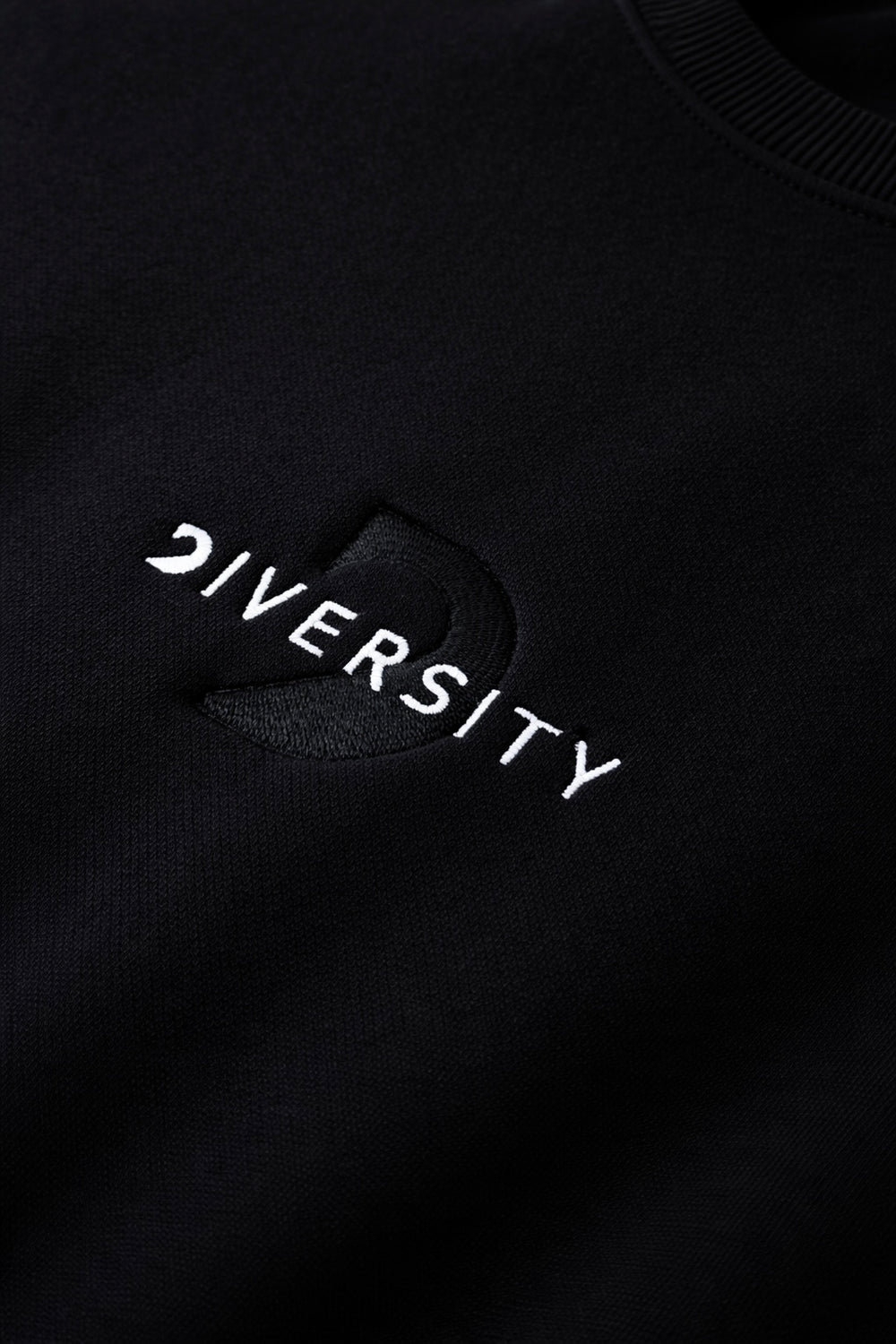 Gros plan du logo DIVERSITY blanc brodé sur un vêtement midweight noir
