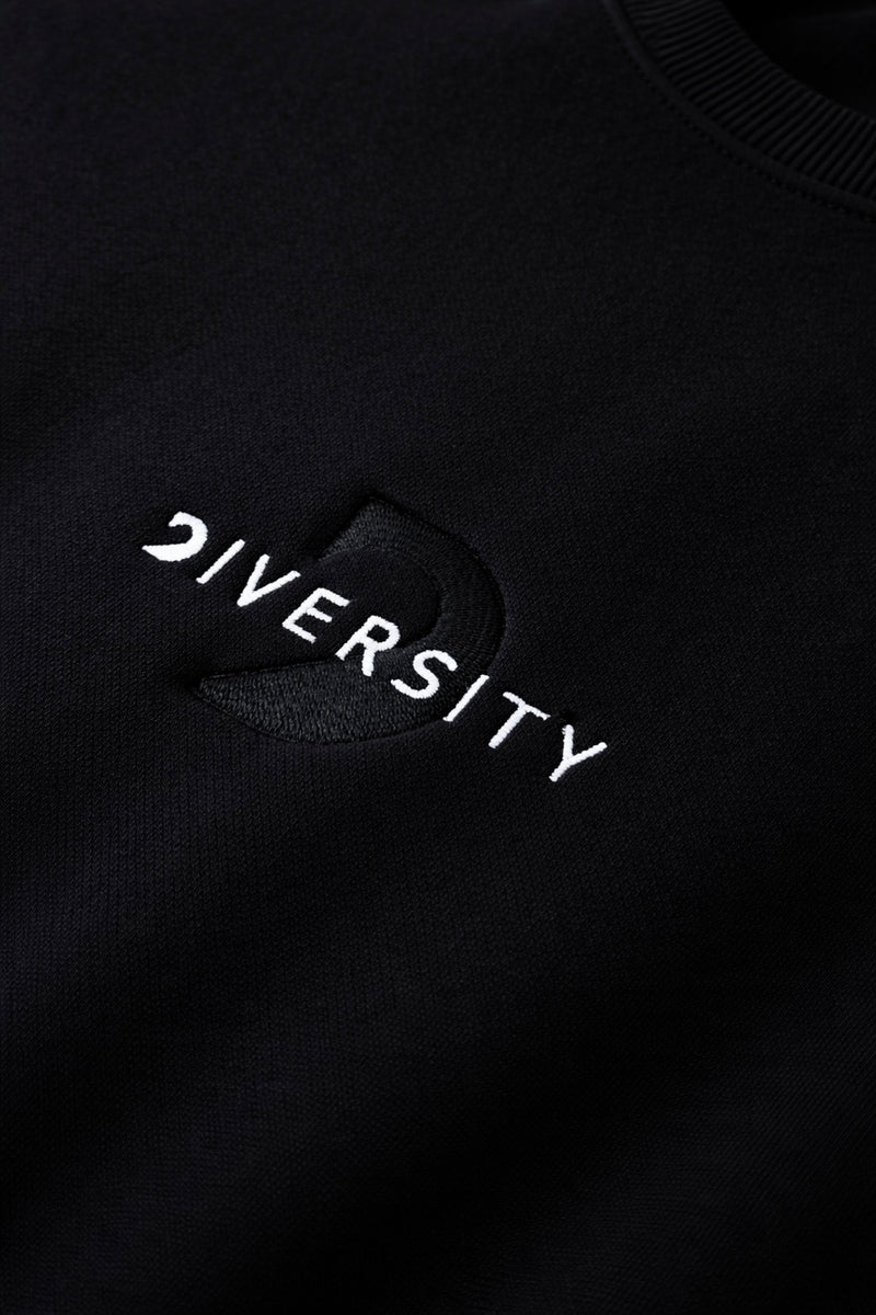 Close-up of the white DIVERSITY logo embroidered on a black midweight piece
