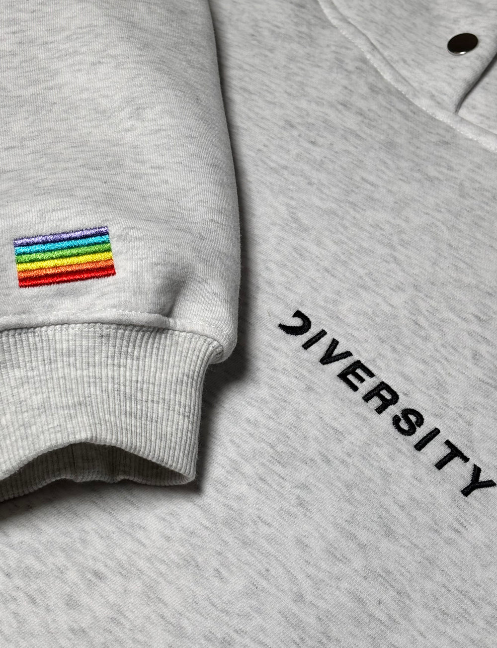 Close-up of the grey Heavyweight Hoodie: rainbow flag embroidered on the sleeve and black DIVERSITY logo