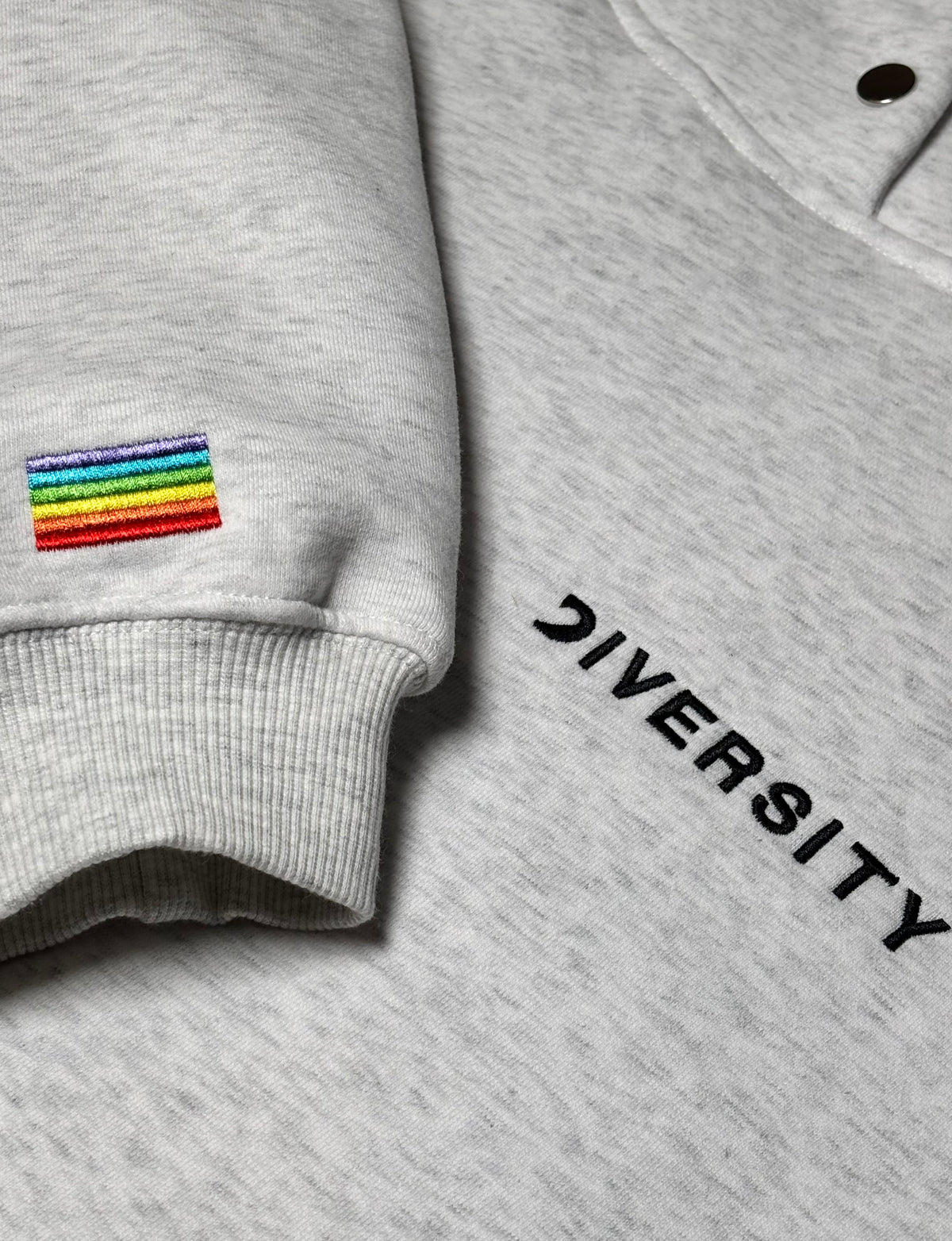 Close-up of the grey Heavyweight Hoodie: rainbow flag embroidered on the sleeve and black DIVERSITY logo