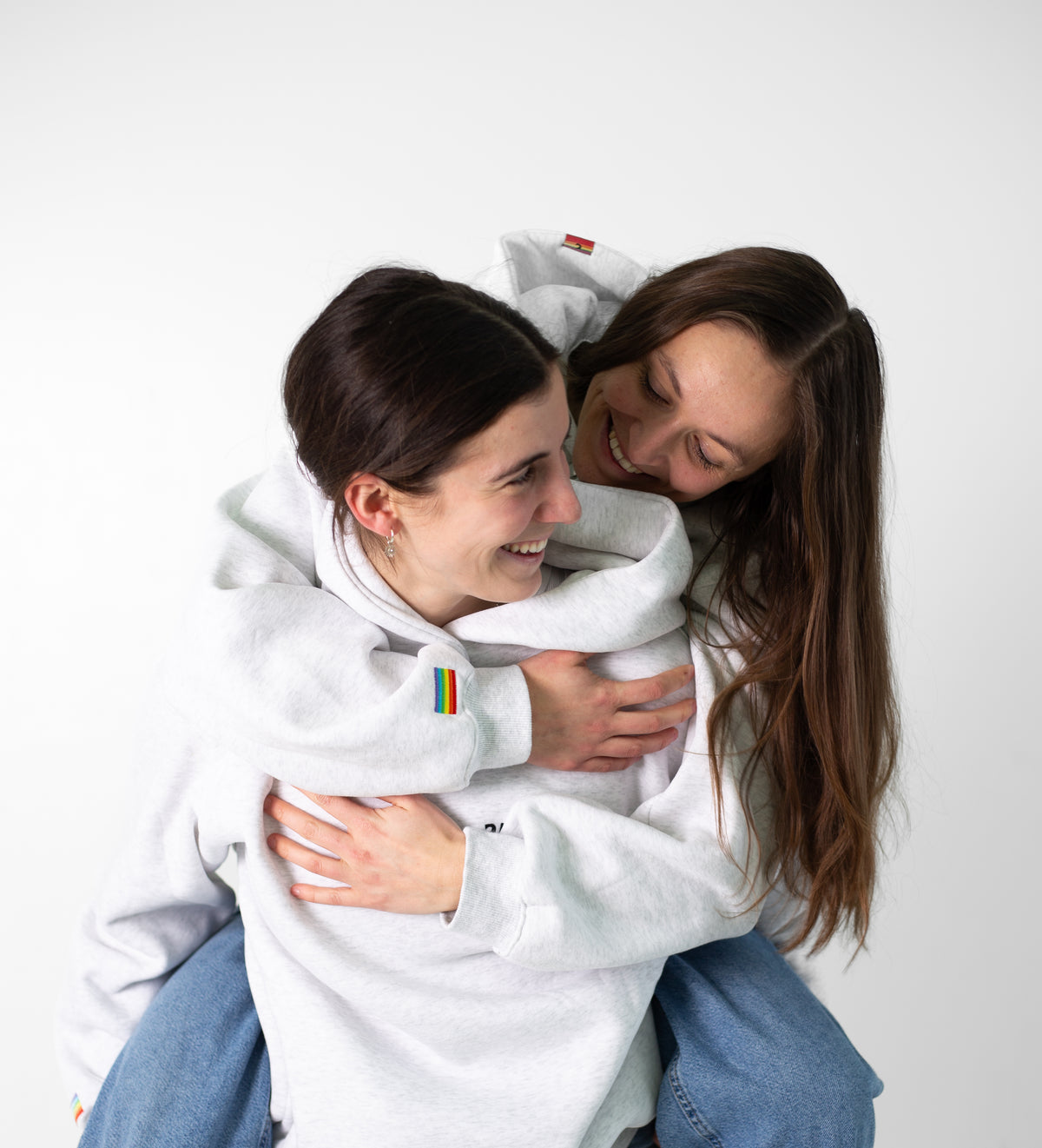 Deux personnes enlacées et souriantes en Heavyweight Hoodie Gris Diversity, drapeau arc-en-ciel sur la manche