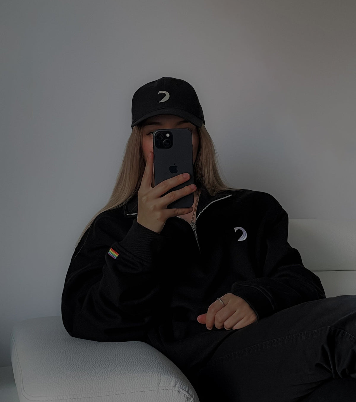 Person wearing the black quarter-zip and a black Diversity cap, mirror selfie