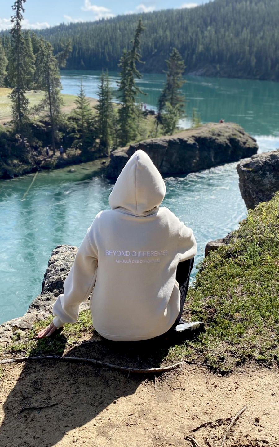 Personne assise au bord d'une rivière, vue de dos, portant le Heavyweight Hoodie Beige Allié