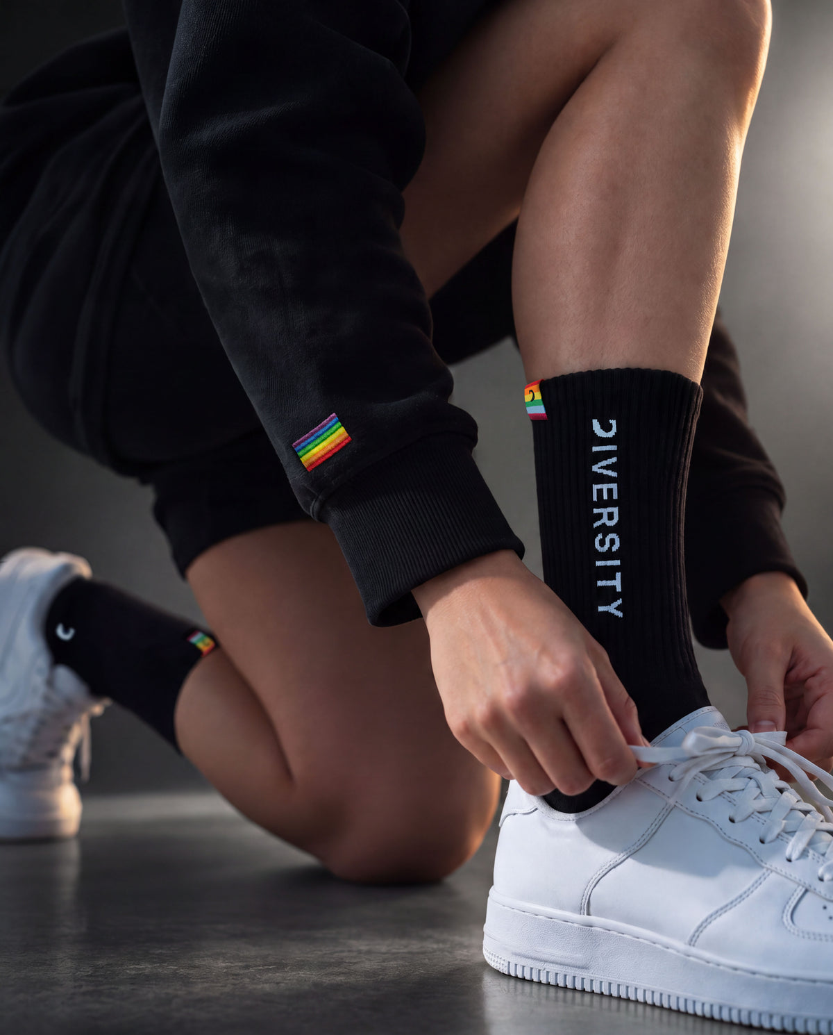 Person tying a white sneaker, black Diversity socks and rainbow flag on the sleeve