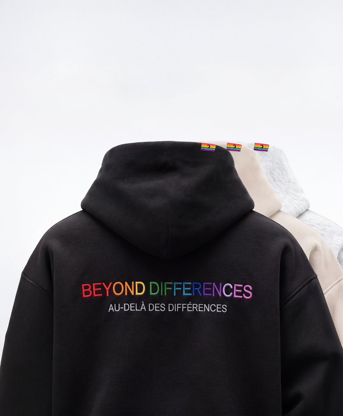 Three Beyond Heavyweight Hoodies seen from the back (black, Sand, grey), BEYOND DIFFERENCES embroidery