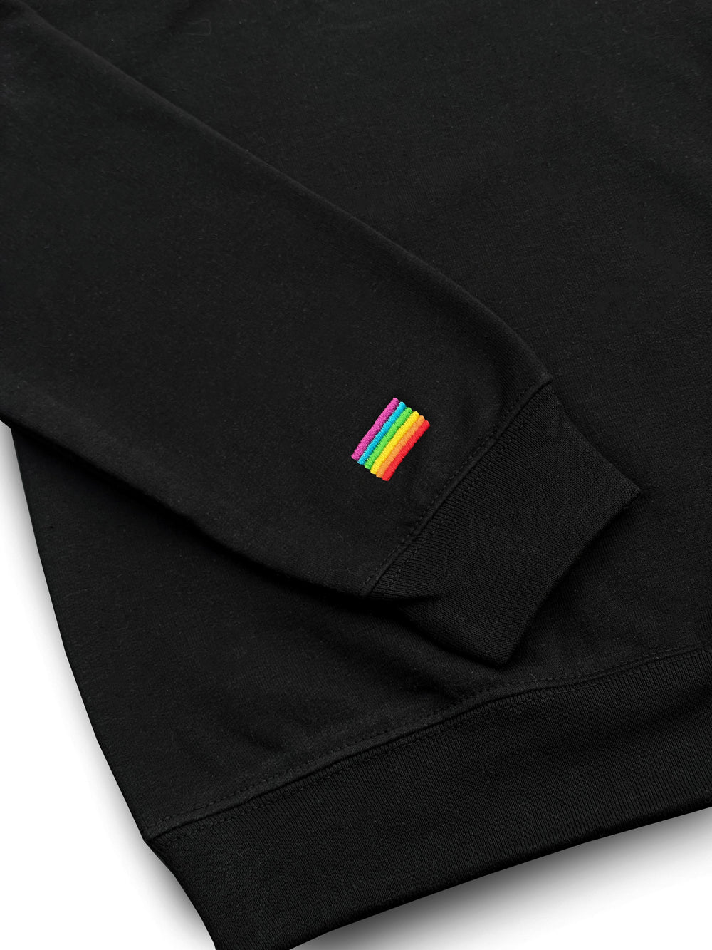 Gros plan du drapeau arc-en-ciel brodé au poignet du chandail 1/4 zip noir